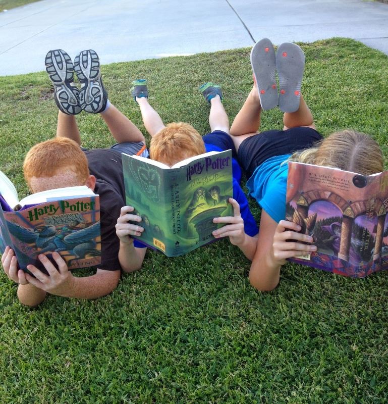 Three kids reading Harry Potter books in grass